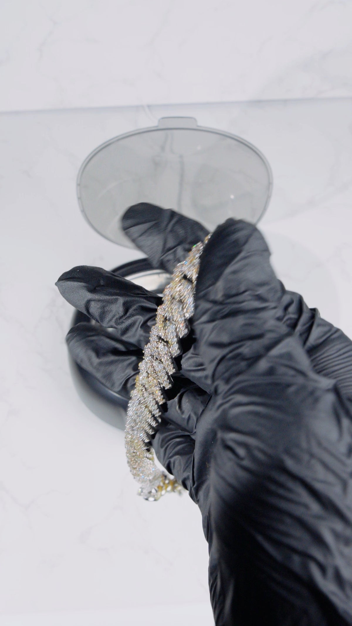 Gloved hands holding a stone-set necklace above SONIQ Clean